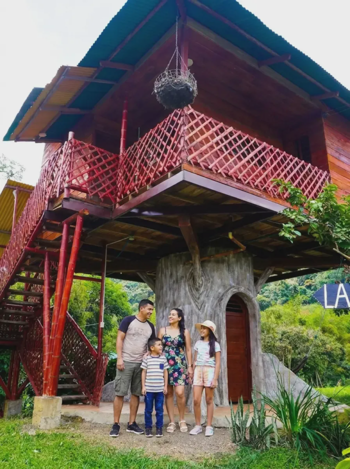 Familia frente a la Cabaña en el Árbol de la Finca La María, con su tronco y escalera roja